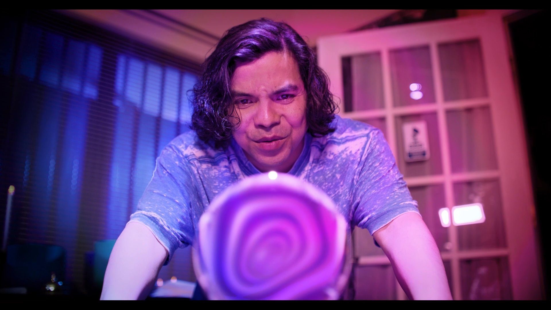 A group of individuals engages in a mysterious ritual involving a glowing crystal ball to perform a psychic divination. The setting is illuminated with deep purple tones, emphasizing the supernatural atmosphere as an image appears within the sphere.