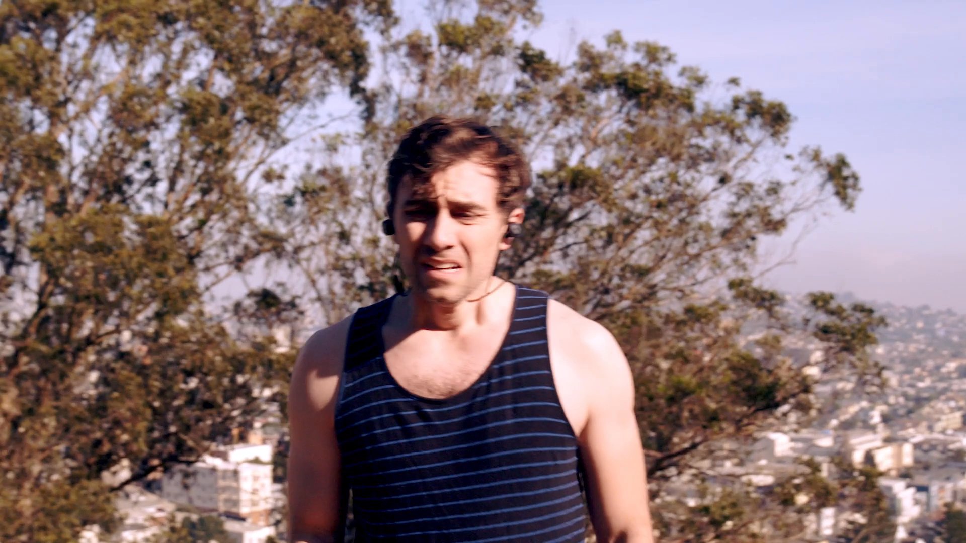 A man experiences significant fatigue while running along a hillside trail, eventually stopping to catch his breath. The scene transitions from intense exertion to a recovery pause in a scenic outdoor environment.