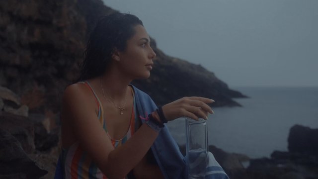 A girl sitting at the beach and drinking water