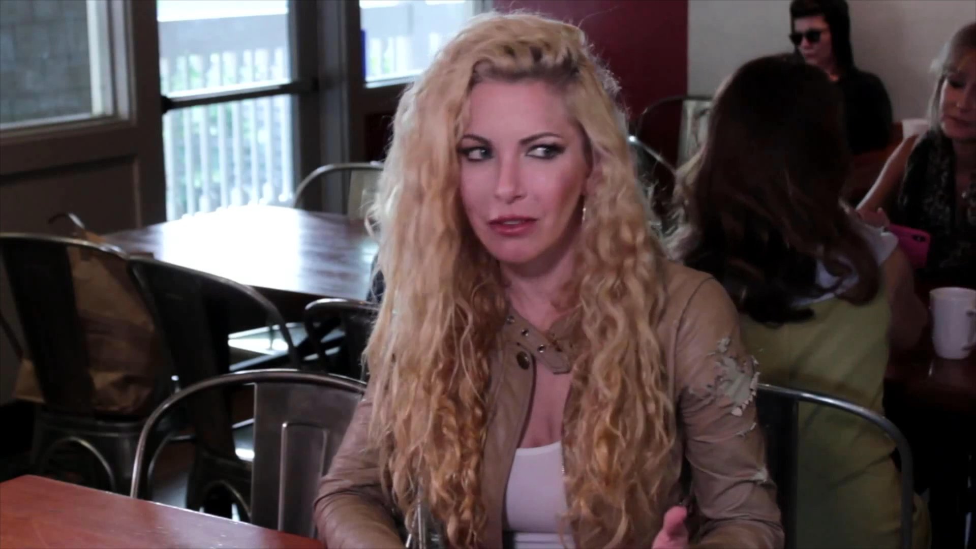 A man and woman engage in a serious, focused conversation while seated at a restaurant booth. The scene features alternating close-up shots as they exchange dialogue in an indoor dining environment.