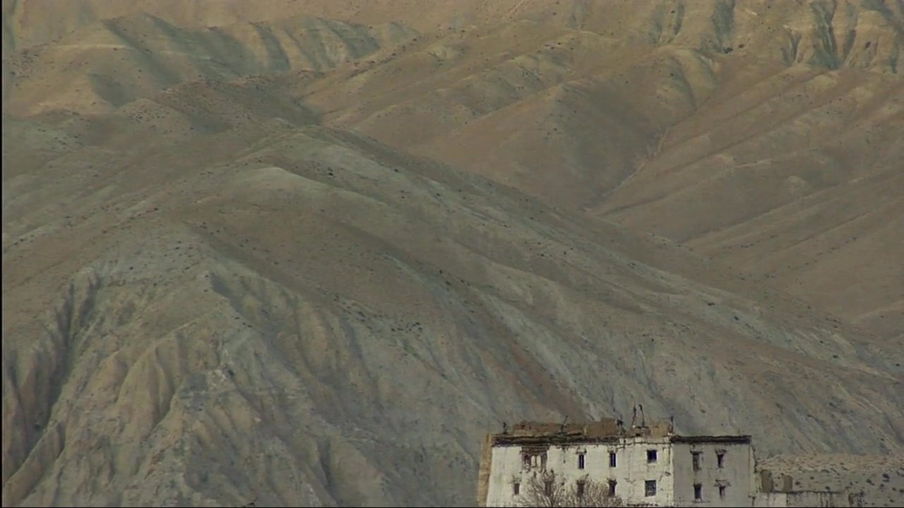 Dramatic mountain peaks transition to a remote monastery village where a local herdsman guides his flock of goats through stone-walled paths.