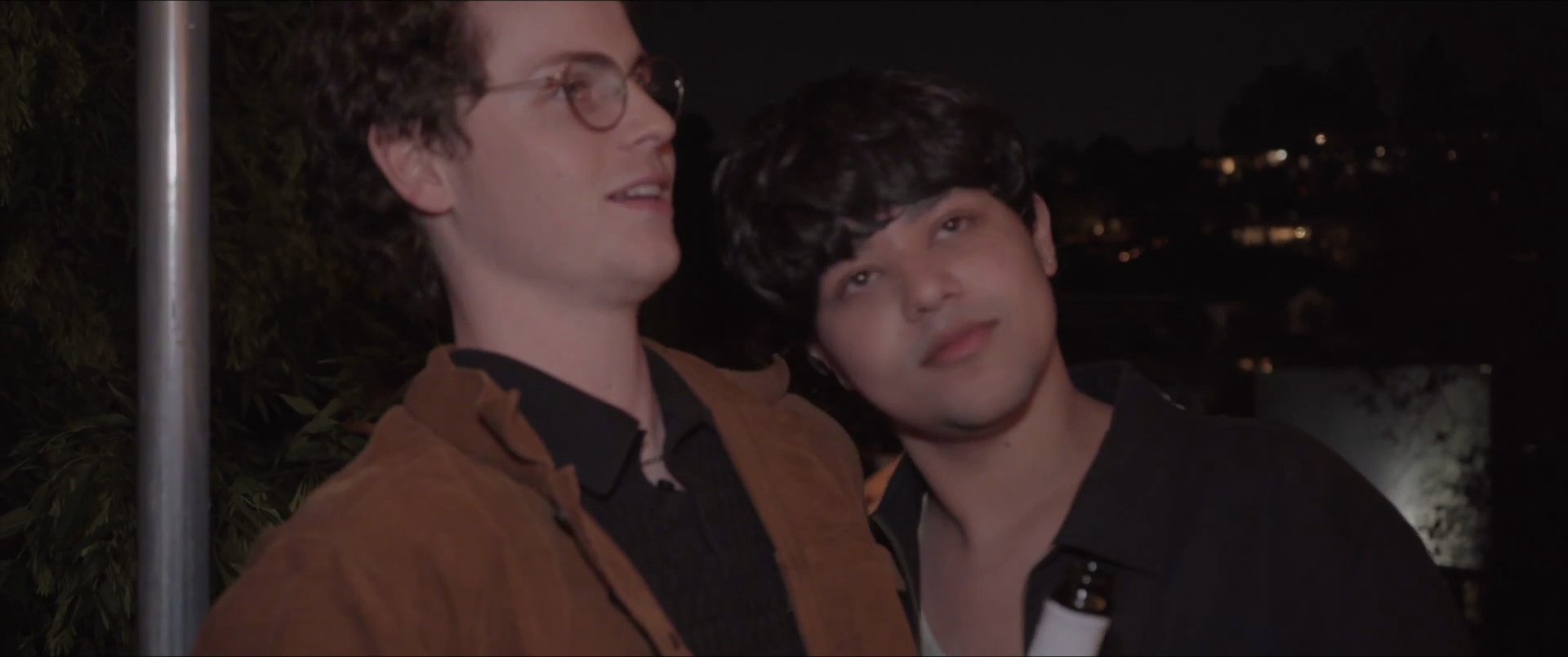 Two friends watch a vibrant fireworks display at night, sharing an intimate and joyful moment together while holding a bottle.