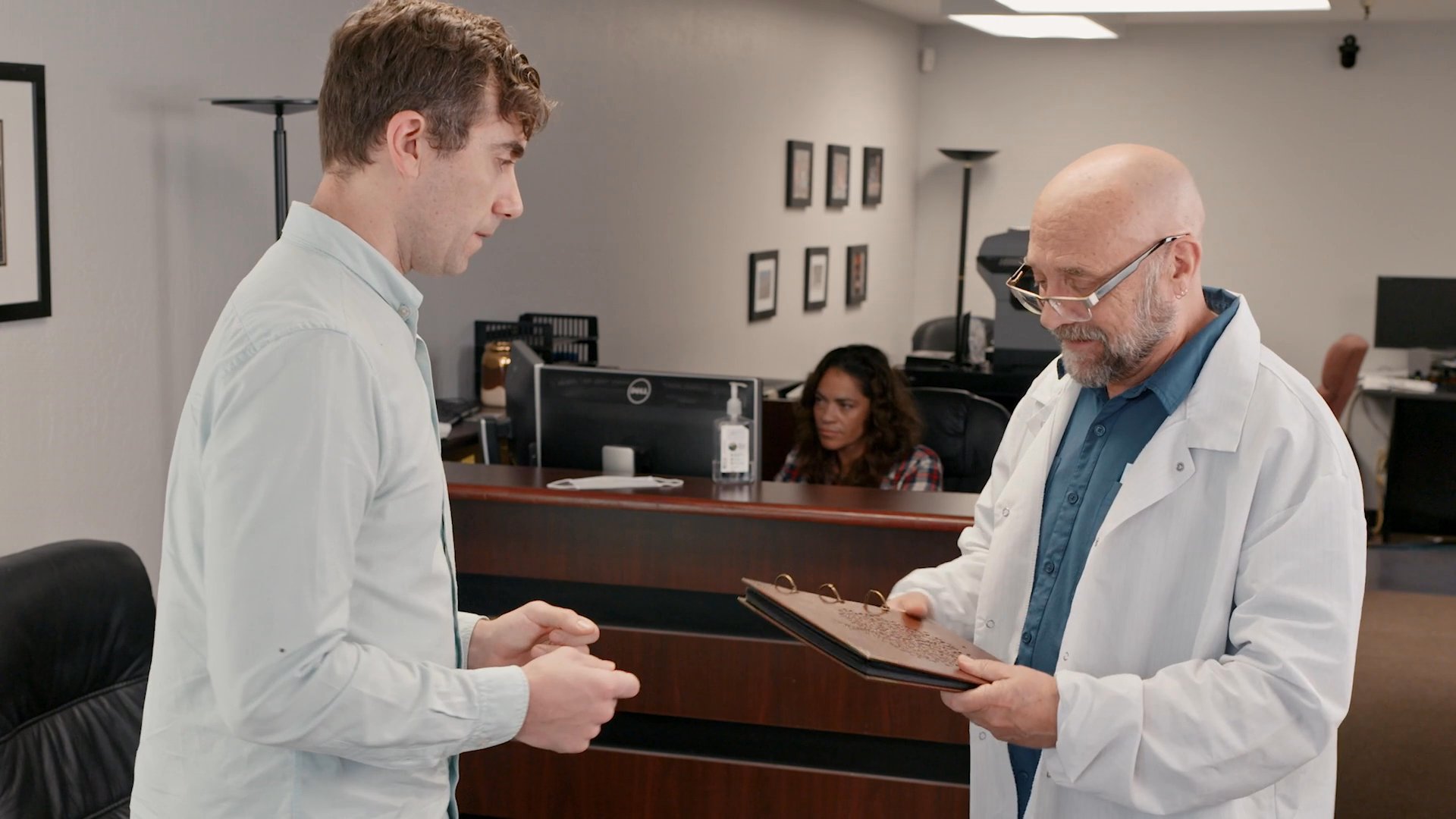 A man in a white coat reviews a document with a patient in an office setting. The interaction involves a discussion regarding the provided materials.