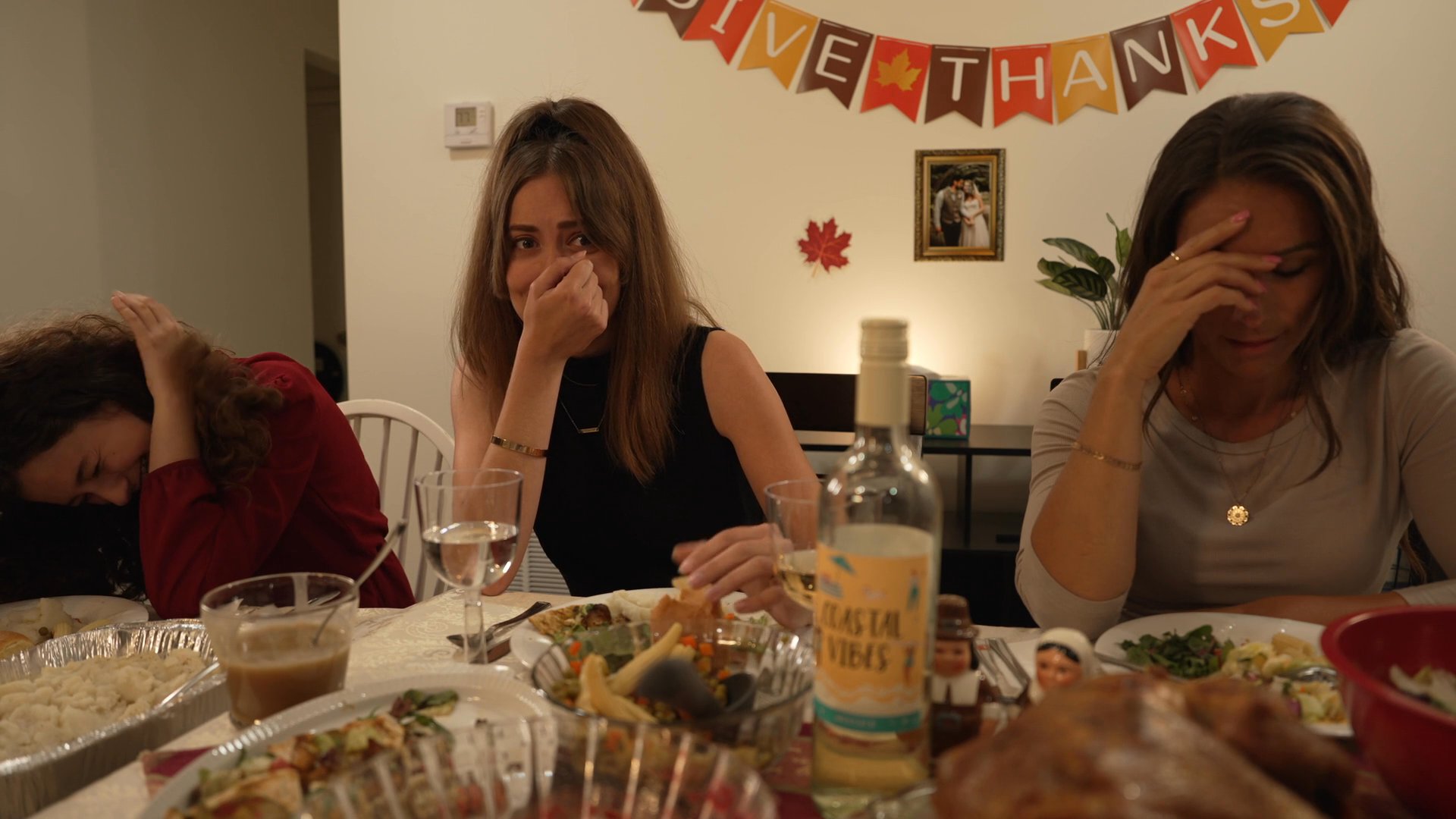 Friends gather for a Thanksgiving dinner, transitioning from informal kitchen conversations to seated group interaction at the dining table.