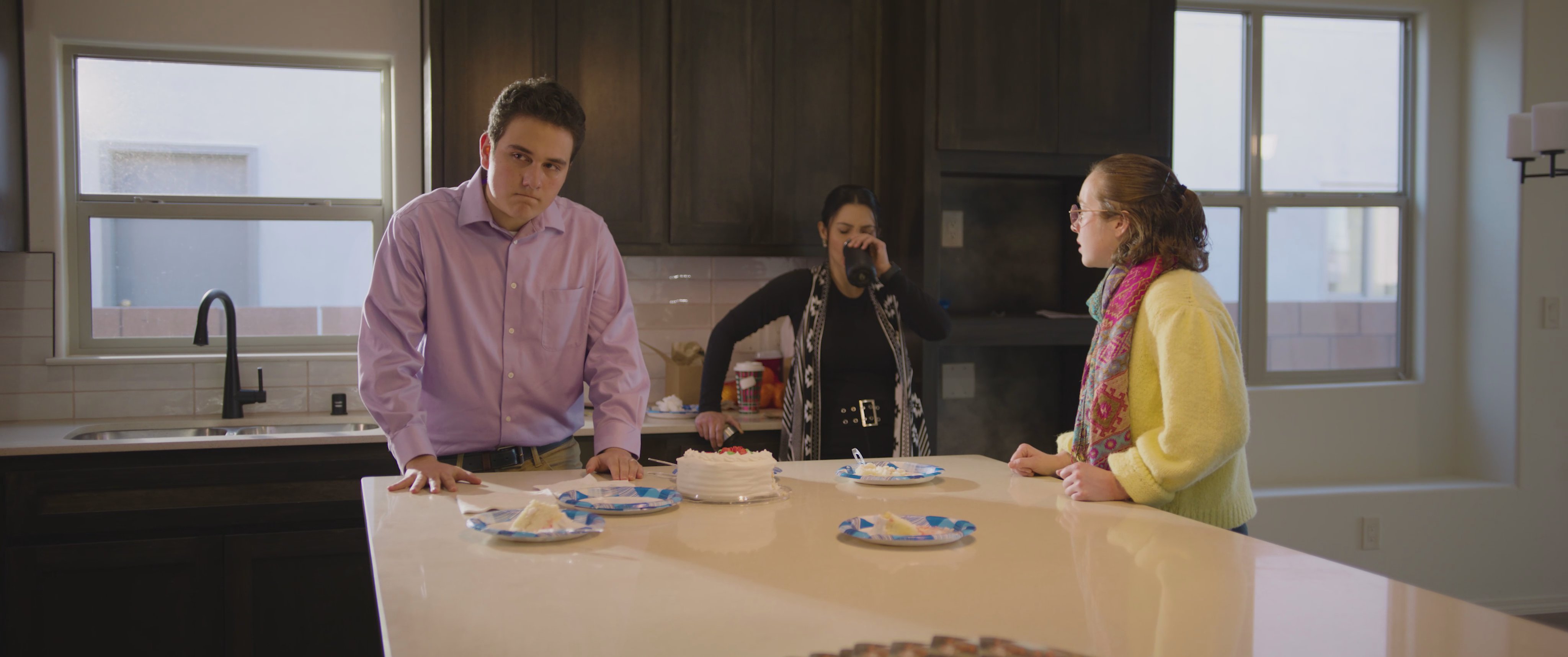 A man engages in a tense conversation with a group in a kitchen, followed by a close-up of a woman expressing emotional distress.