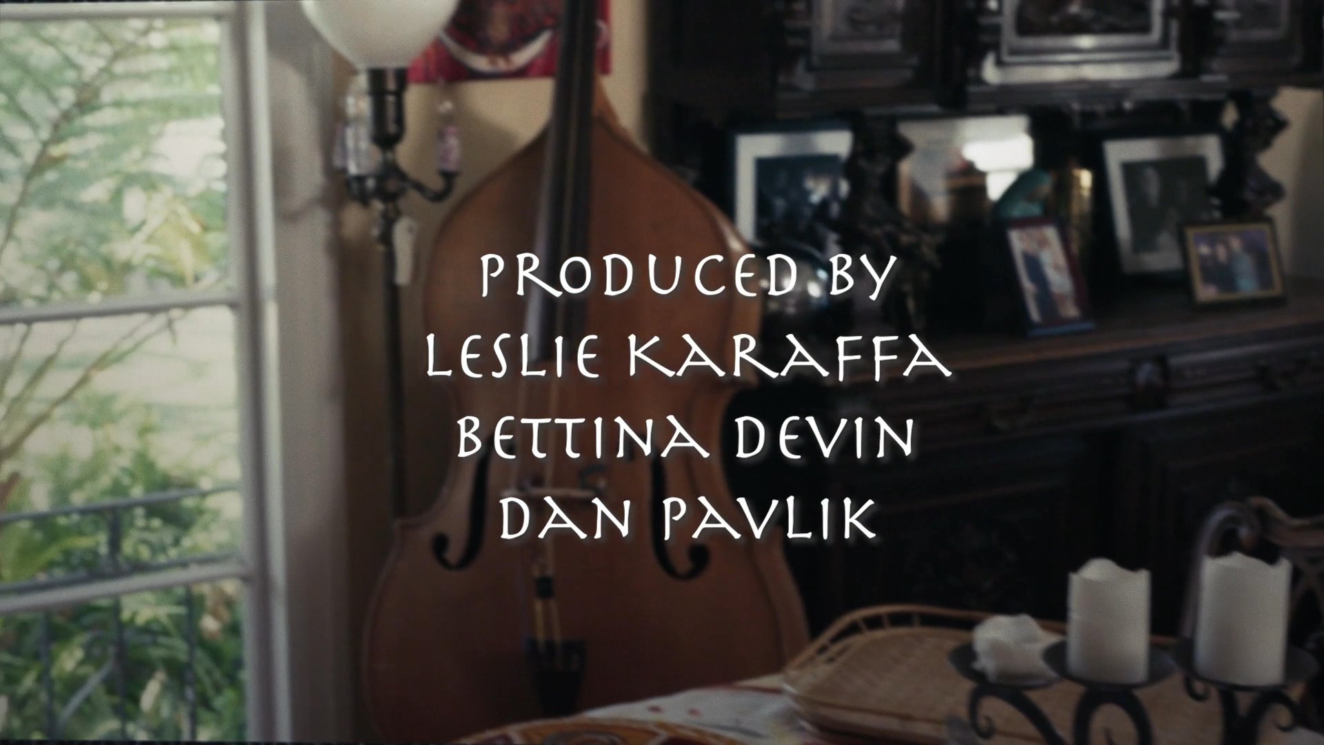Production credits appear over a softly lit interior scene featuring a dining table adorned with mystical decor, candles, and framed family photographs.