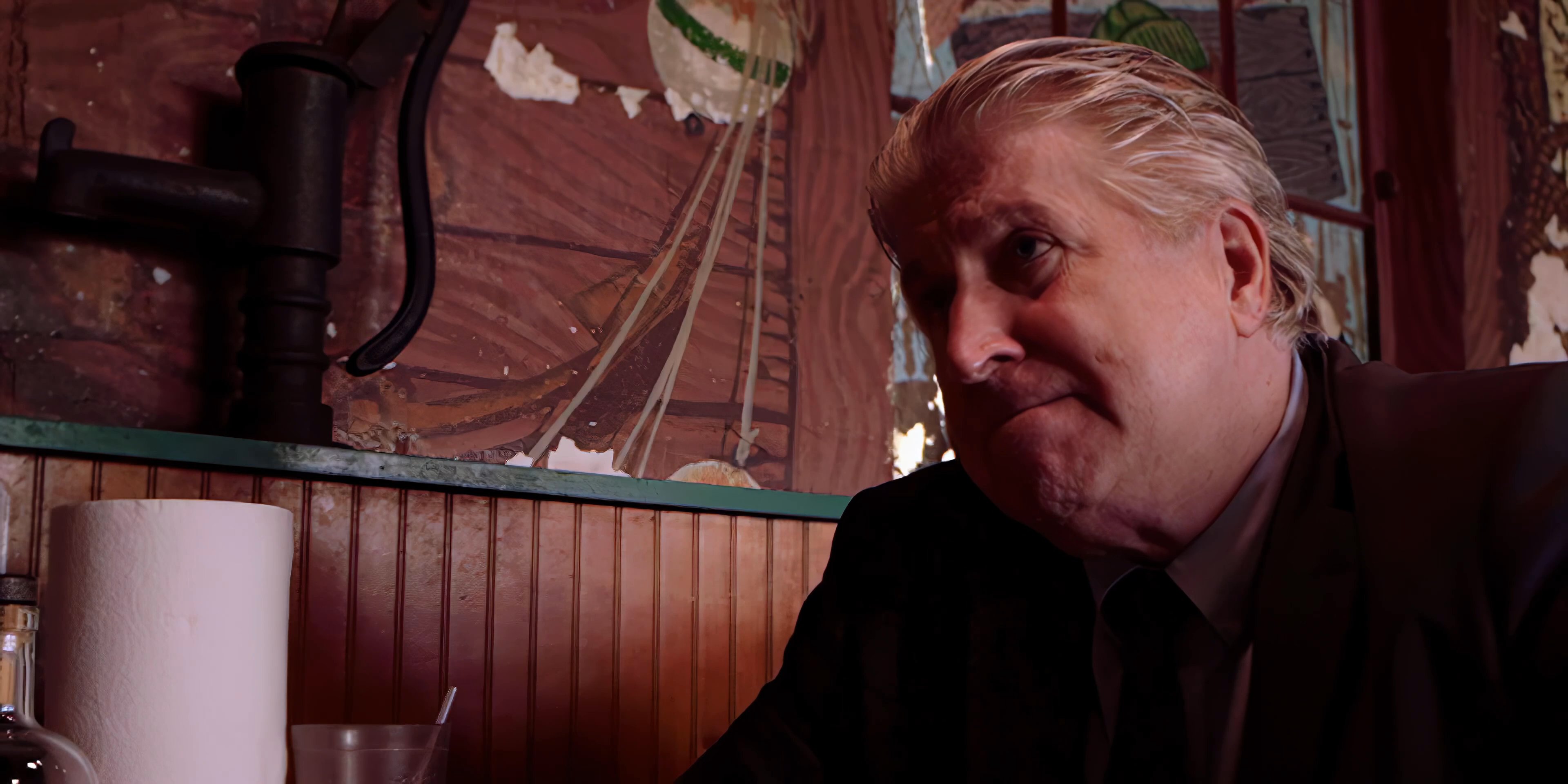 Two men engage in an intense, gestural conversation while seated at a table in a dimly lit, rustic diner.
