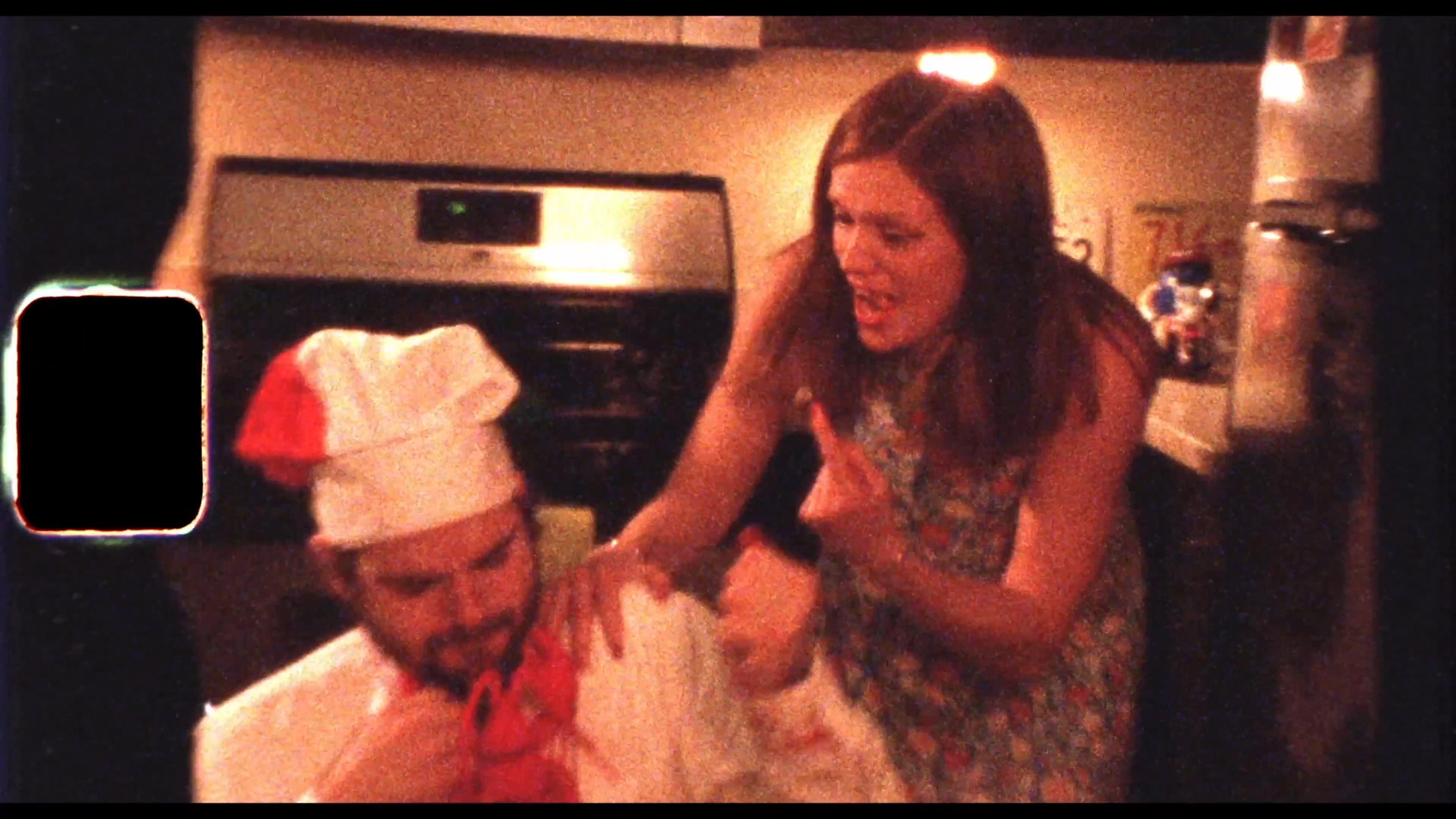 A chaotic dinner scene escalates as a man in a chef's hat struggles with a lobster, eventually involving a chainsaw in a surreal, slapstick sequence.