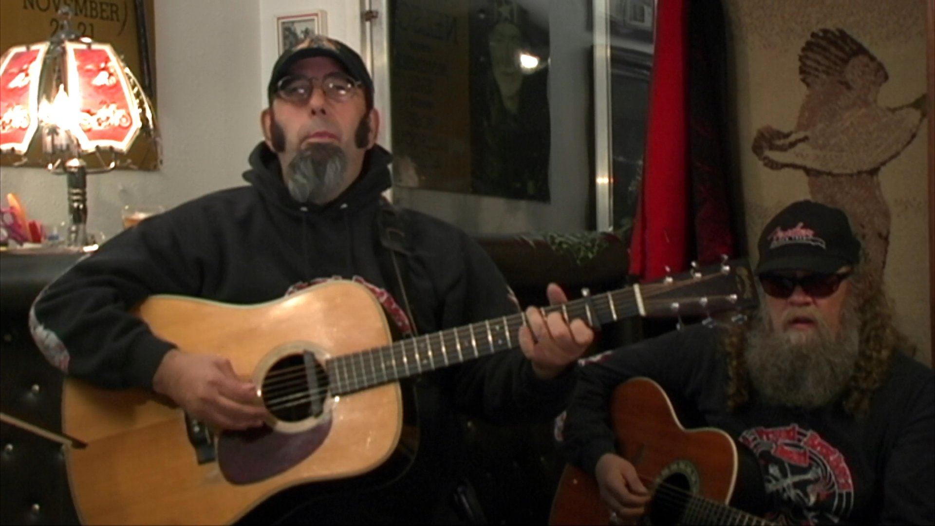 Two musicians perform an acoustic arrangement featuring guitar and fiddle accompaniment in an indoor setting.