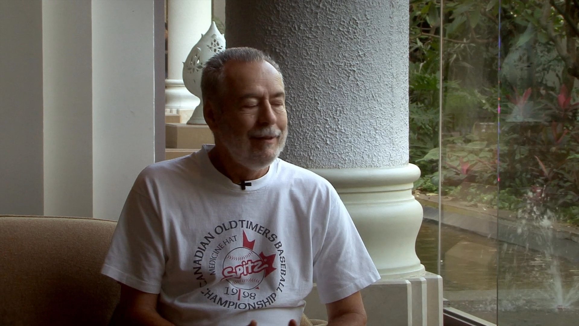 An older man sits comfortably in an indoor setting while speaking directly to the camera in a professional interview style.