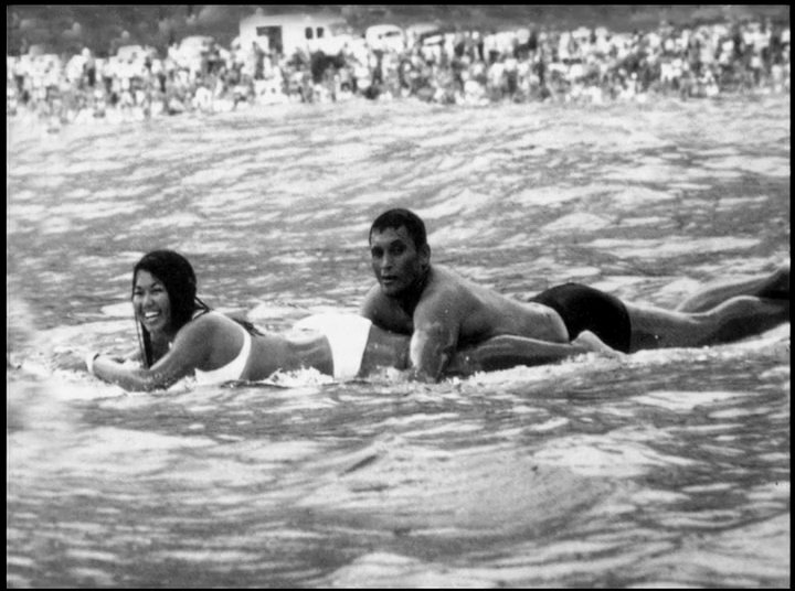 Family home movie footage transitions from black-and-white clips of children and parents enjoying time at the beach to contemporary color shots of the individuals as adults.