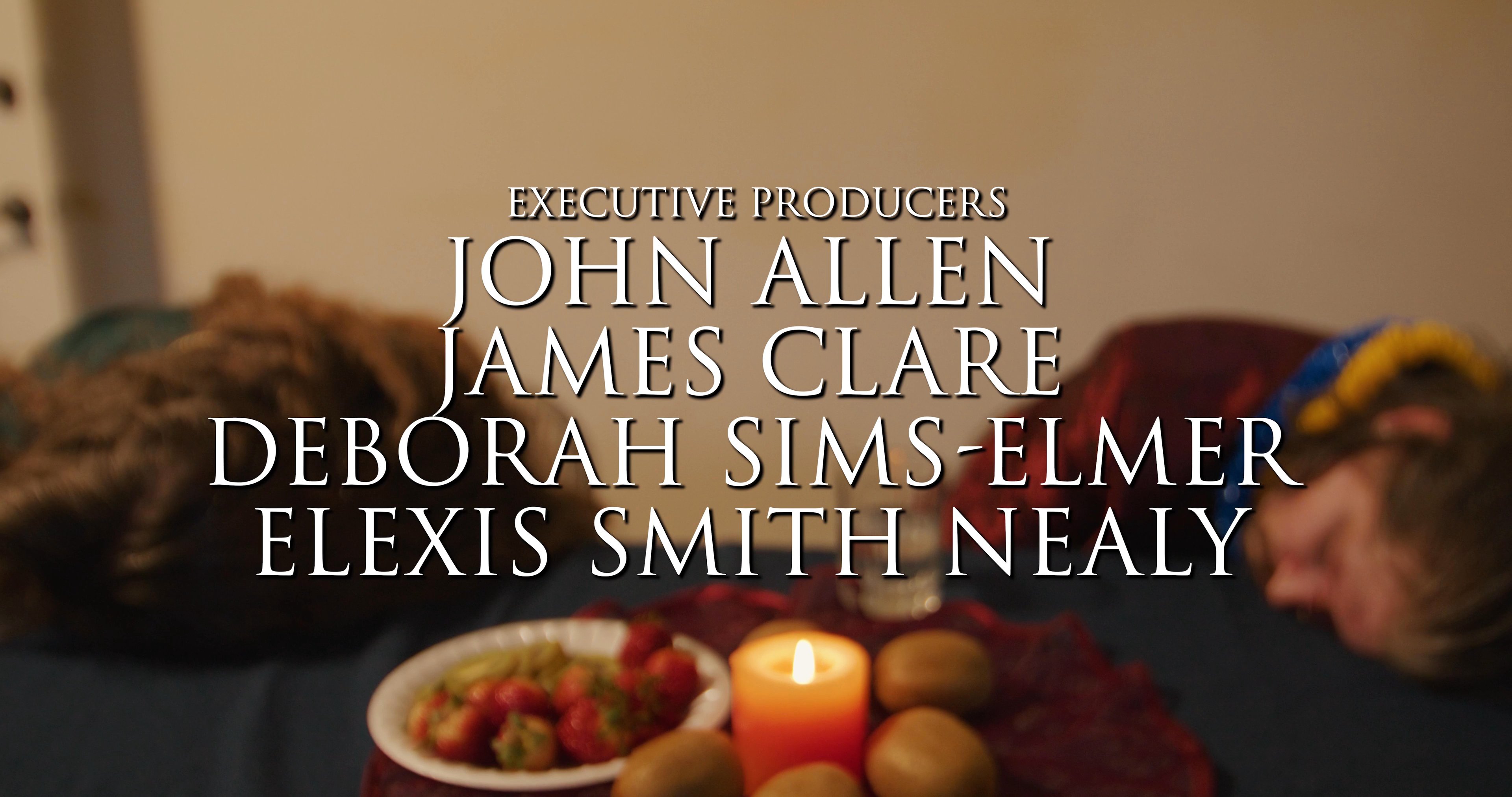 Characters sit at a dimly lit dining table as the opening title and production credits for the film appear on screen.