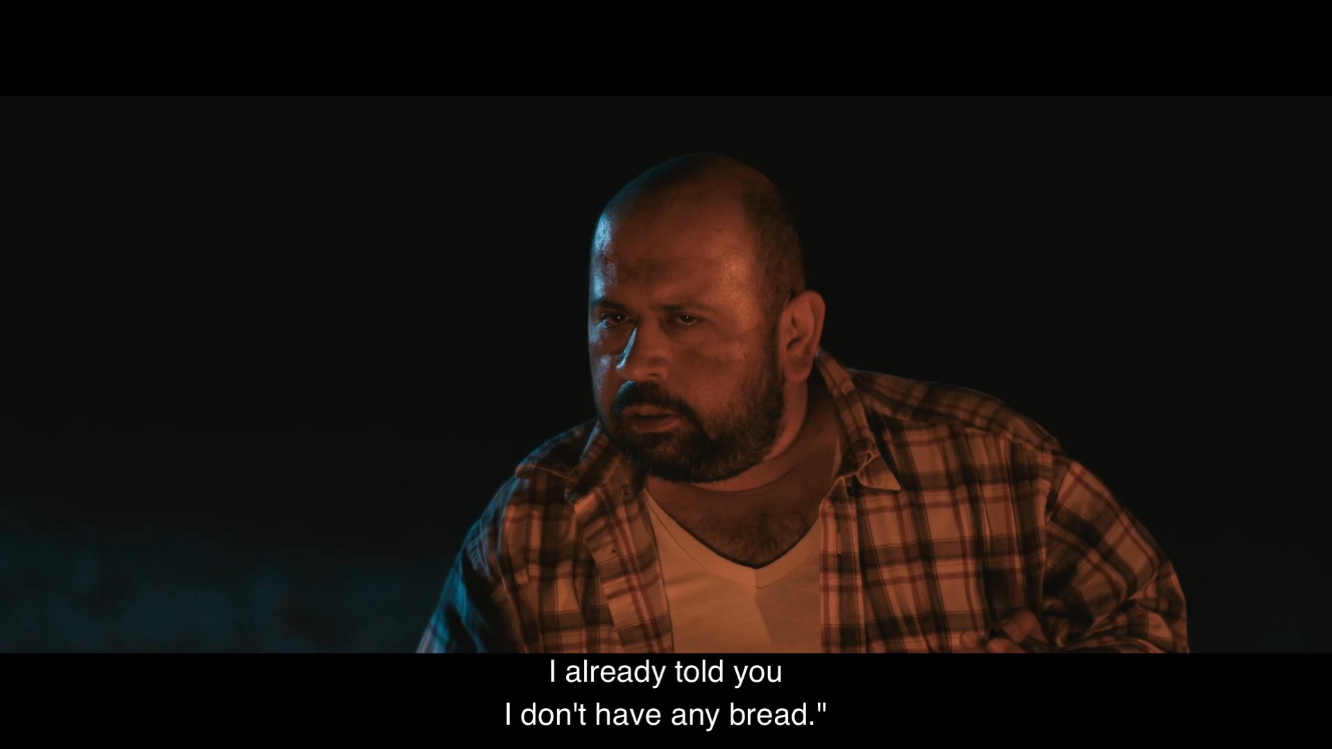 Two men sit together by a campfire at night, engaging in a humorous, repetitive back-and-forth dialogue about bread.