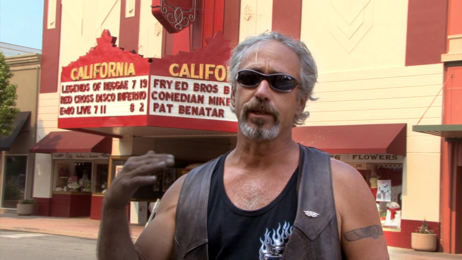 Two men, identified as a band member and a roadie, provide commentary while standing in front of the historic California Theatre.