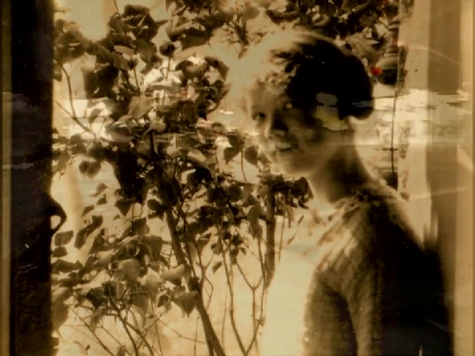 A young child plays in a sandbox, transitioning into a surreal, dreamlike sequence of a woman beside foliage, ending with blurred, light-streaked footage of city streets at night.