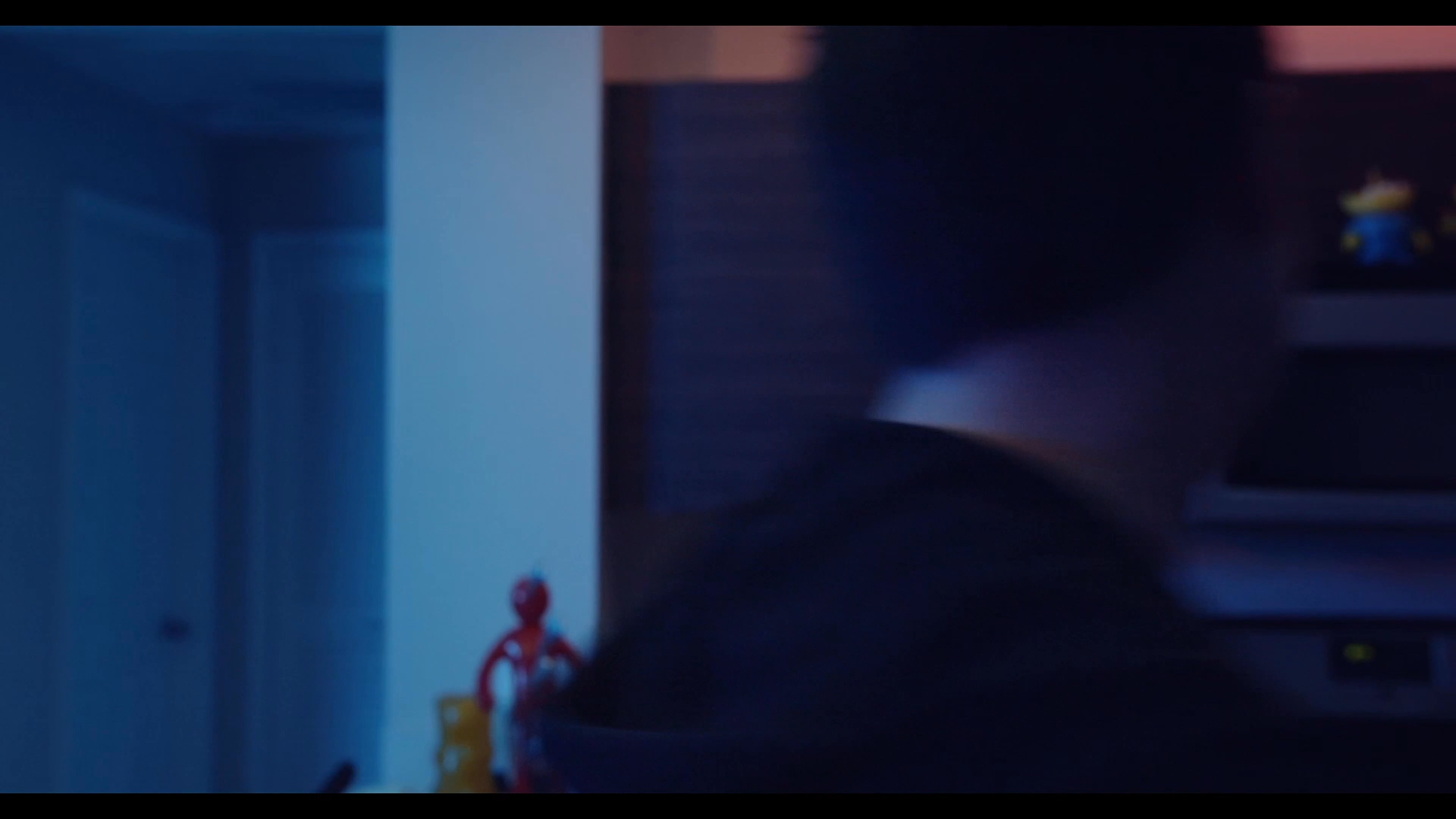 Two men converse in a domestic apartment living area before one moves into the kitchen to search through cupboards.