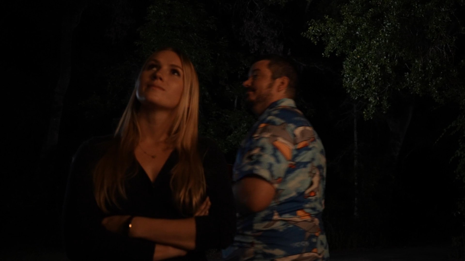 A man and woman engage in conversation while standing outdoors under a clear night sky filled with stars.
