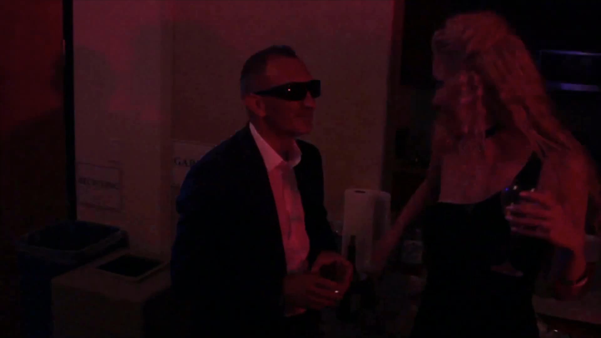 Guests engage in social interaction and dancing during an evening party in an indoor setting. The scene captures the lively atmosphere of the celebration as individuals move to music and mingle with each other.