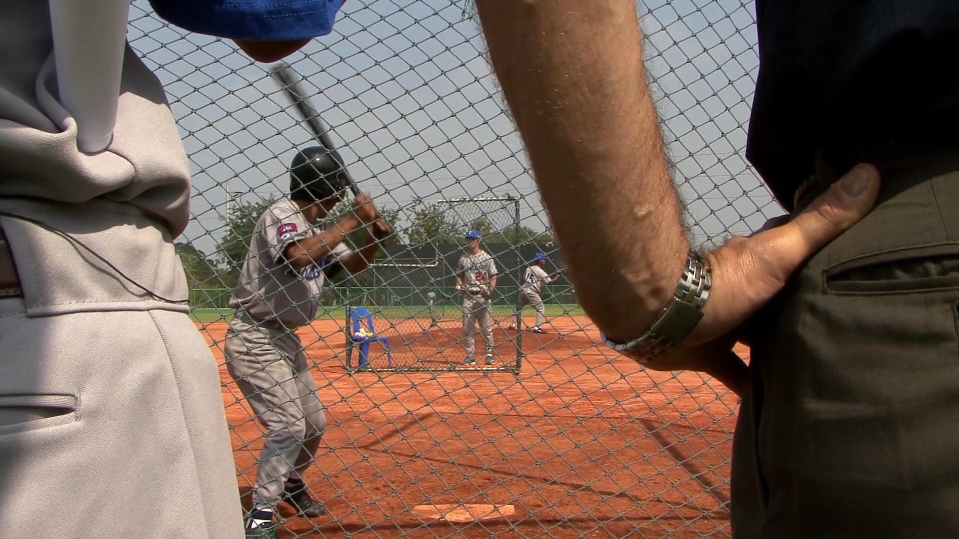An instructor provides professional guidance to a player during an organized baseball batting practice session on an outdoor field.