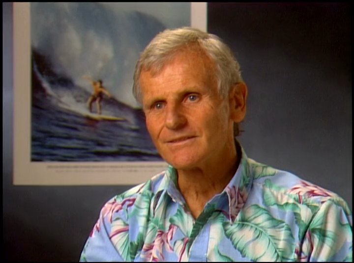 An experienced surfer paddles and navigates through ocean waves, alternating with an interview segment reflecting on the sport. The visual narrative captures both the physical motion of surfing and the personal perspective of the athlete.
