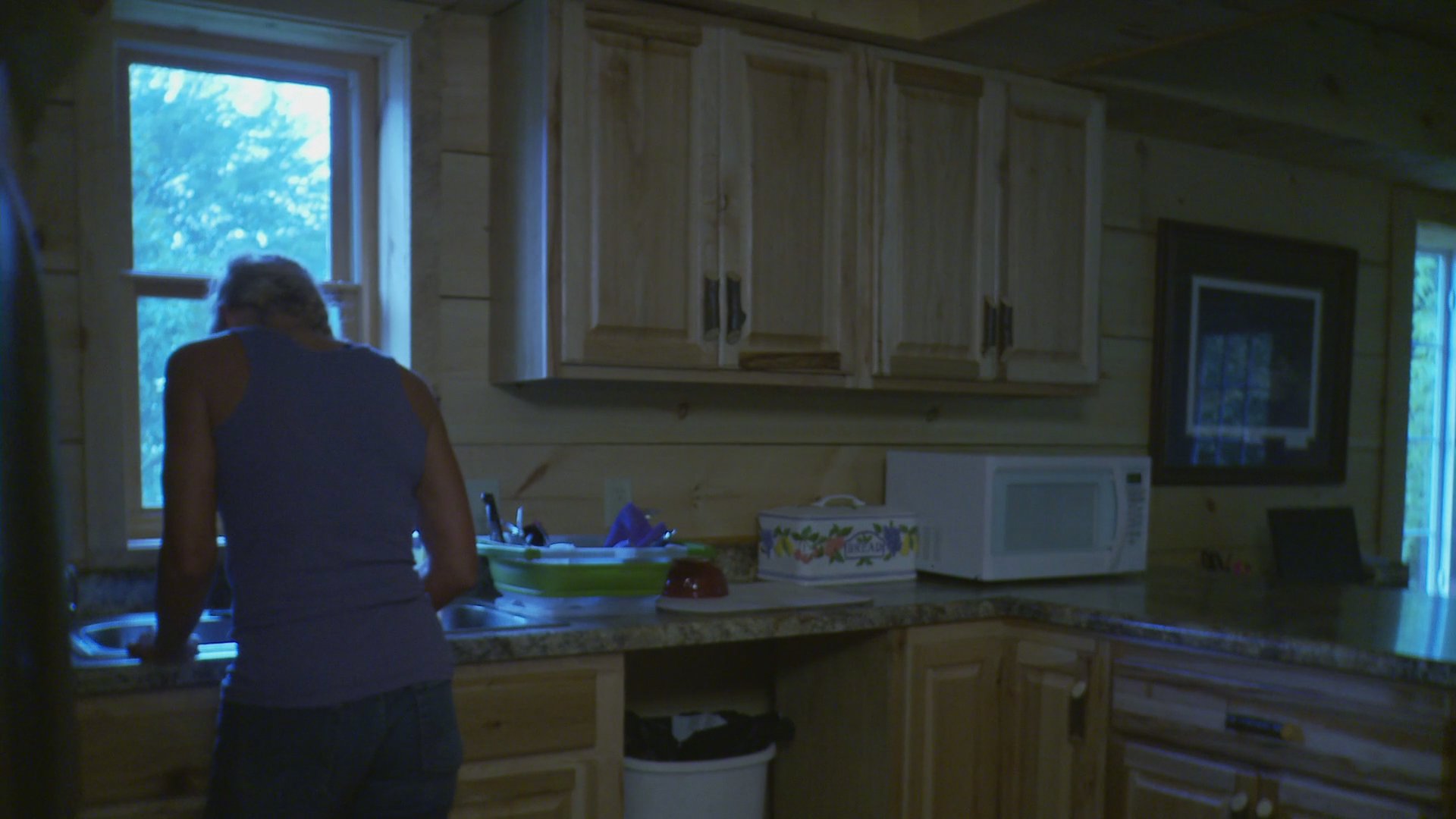 An intense conversation unfolds between a woman in a kitchen before shifting to a somber discussion between a young woman and an older man in a living room. The sequence captures a shift from personal distress to a quiet, emotionally heavy family interaction.