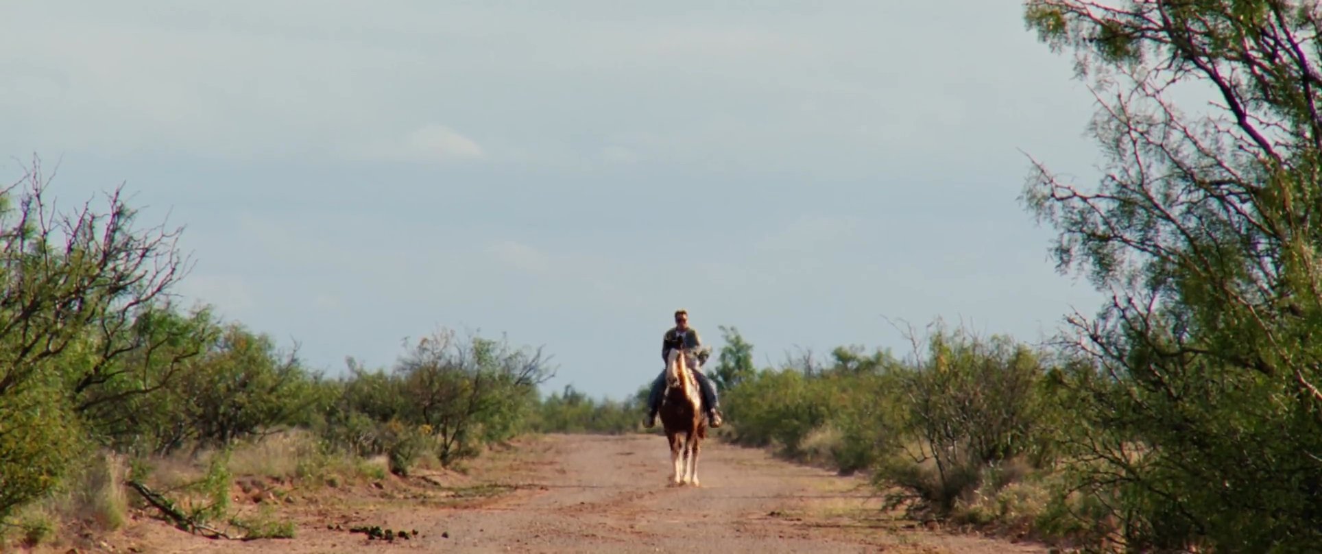 An instructor guides a novice rider through mounting and maneuvering a horse along a desert path.
