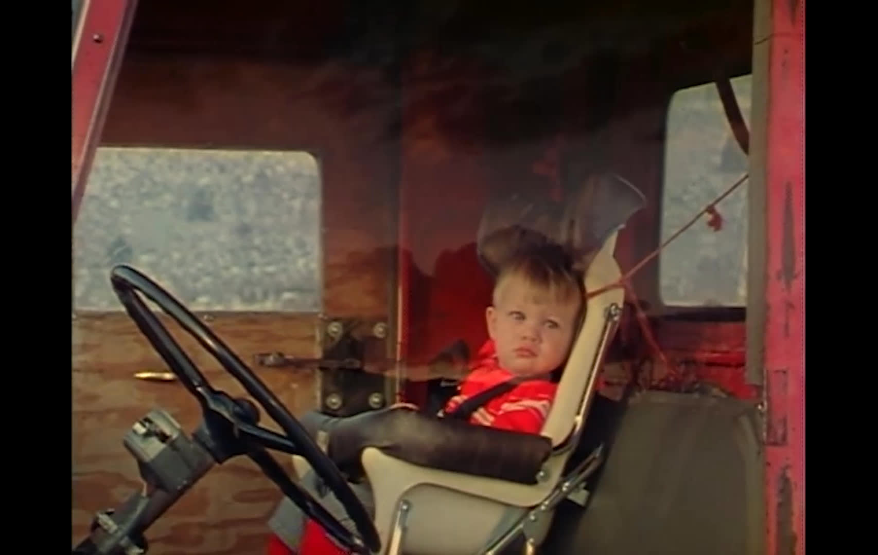 A woman in a knit hat operates a farm vehicle while a young child rides nearby, with ranch chores and a sunset landscape appearing around them. She reflects on her grandson Jeff becoming a rancher and imagines a future of healthy cattle, rain, and good hay crops.
