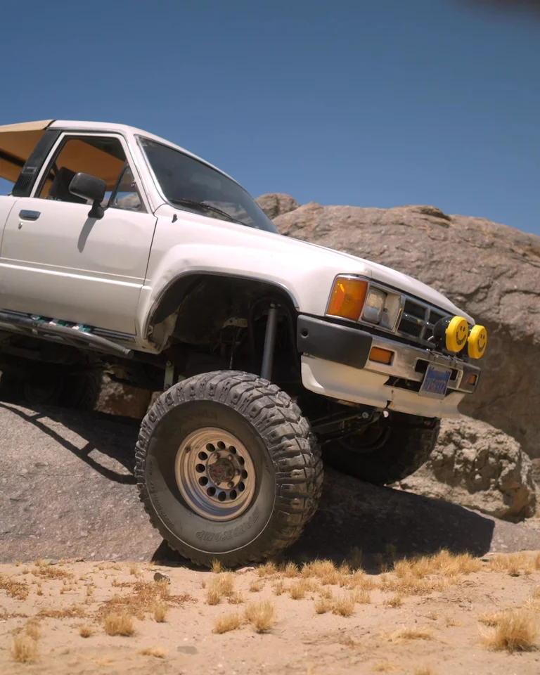Truck driving over large boulder in the desert