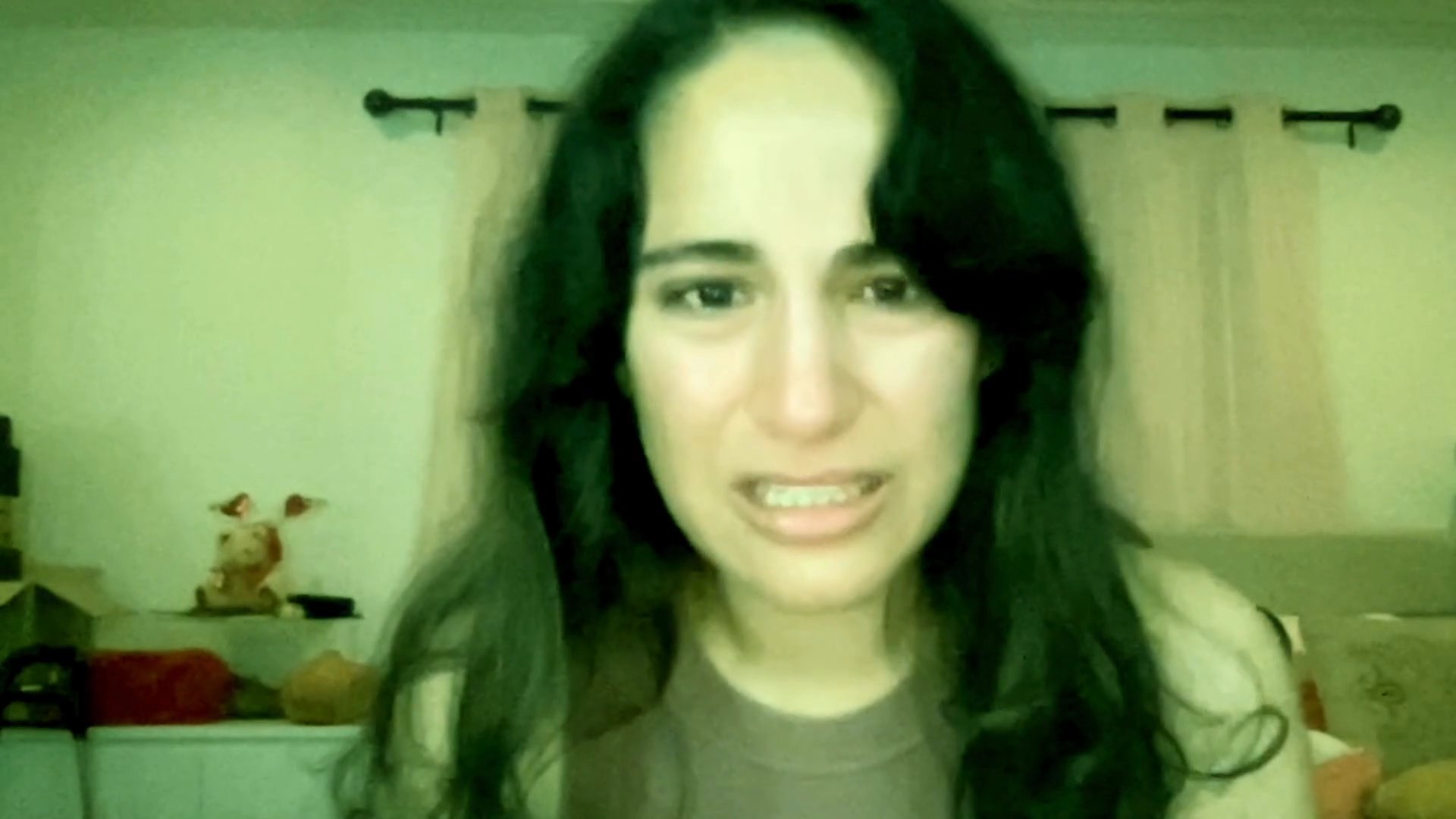 A woman sits in a bedroom and tearfully shares a personal account of emotional distress directly to the camera. Her expressions fluctuate between intense sorrow, vulnerability, and active communication.