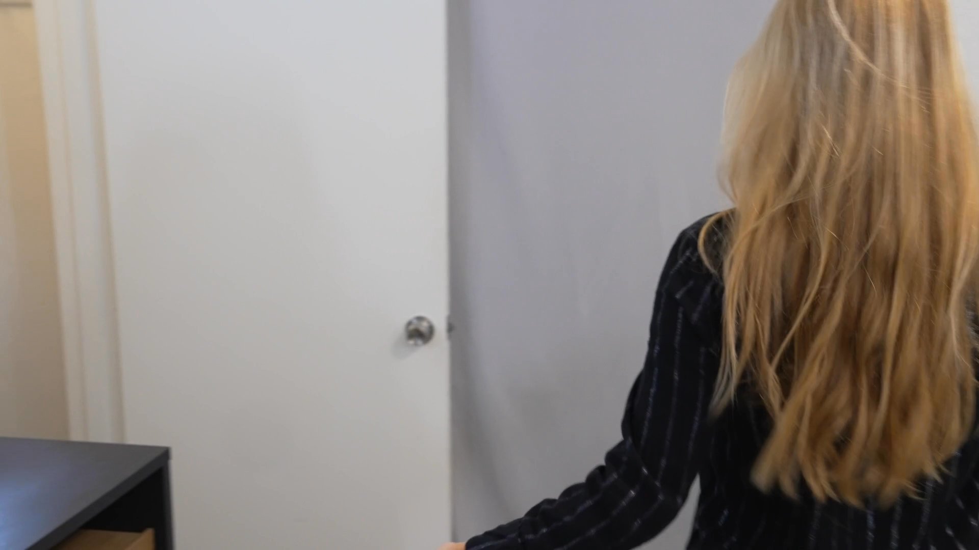 A woman in pajamas wakes up in her bedroom before transitioning to stand and engage in an active explanation to an off-camera audience.