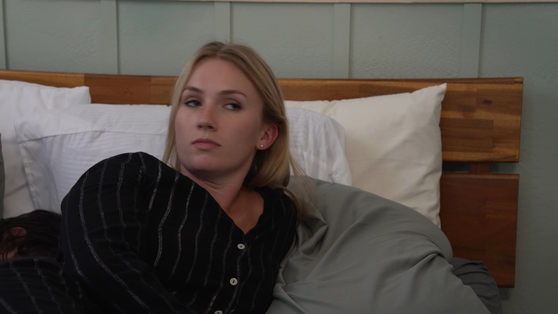 A woman wakes up in bed beside her partner and leaves the room to write a note, signaling interpersonal tension.