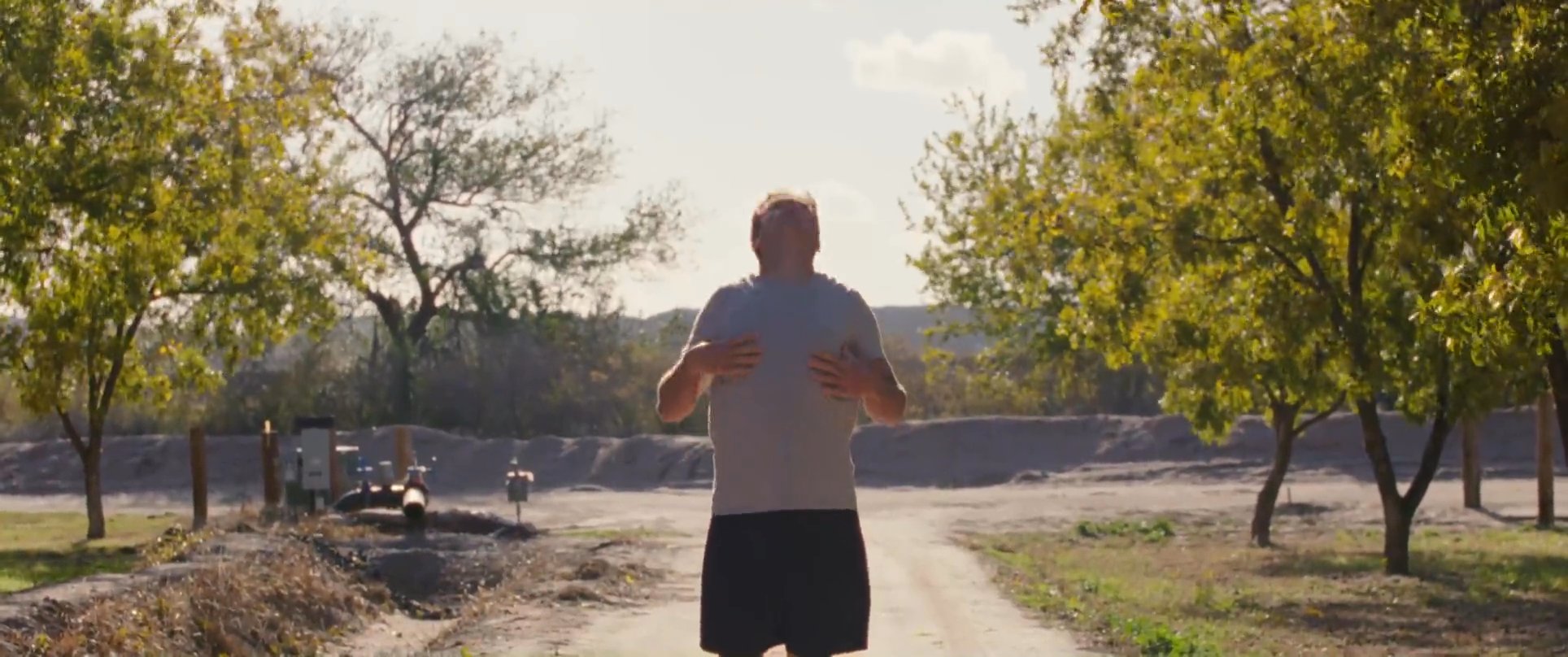An athlete jogs through an outdoor orchard before transitioning to a reflective conversation with an older man. The scene concludes with a focus on flowing water, symbolizing movement and tranquility.