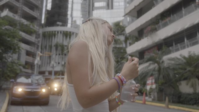 Blonde girl standing in between buildings while drinking water