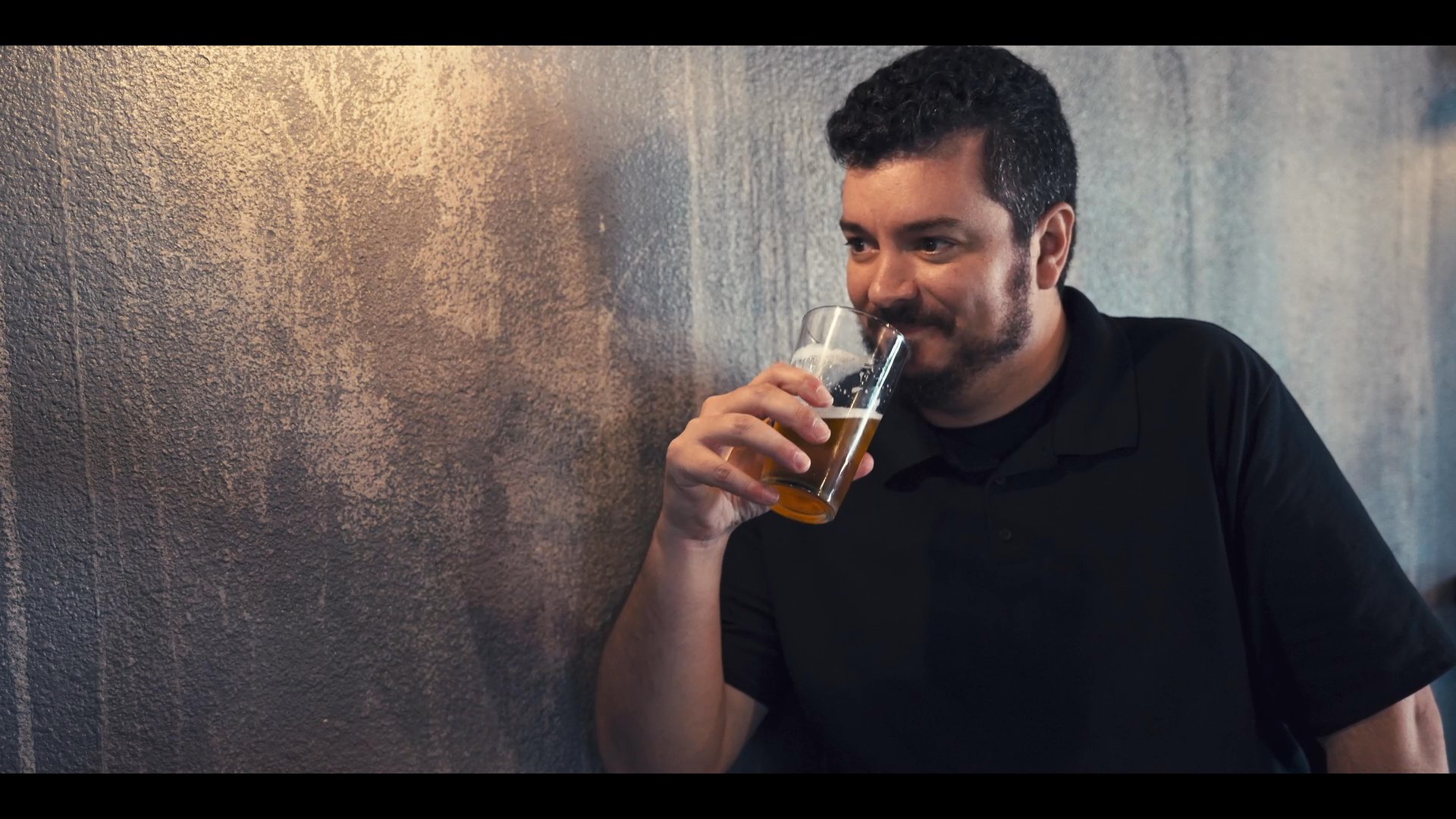 Two men engage in an animated conversation while sitting at a bar and drinking beer. They exchange thoughts and gestures, illustrating a casual social interaction.