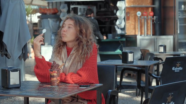 A girl is eating chocolate ice cream in a street cafe