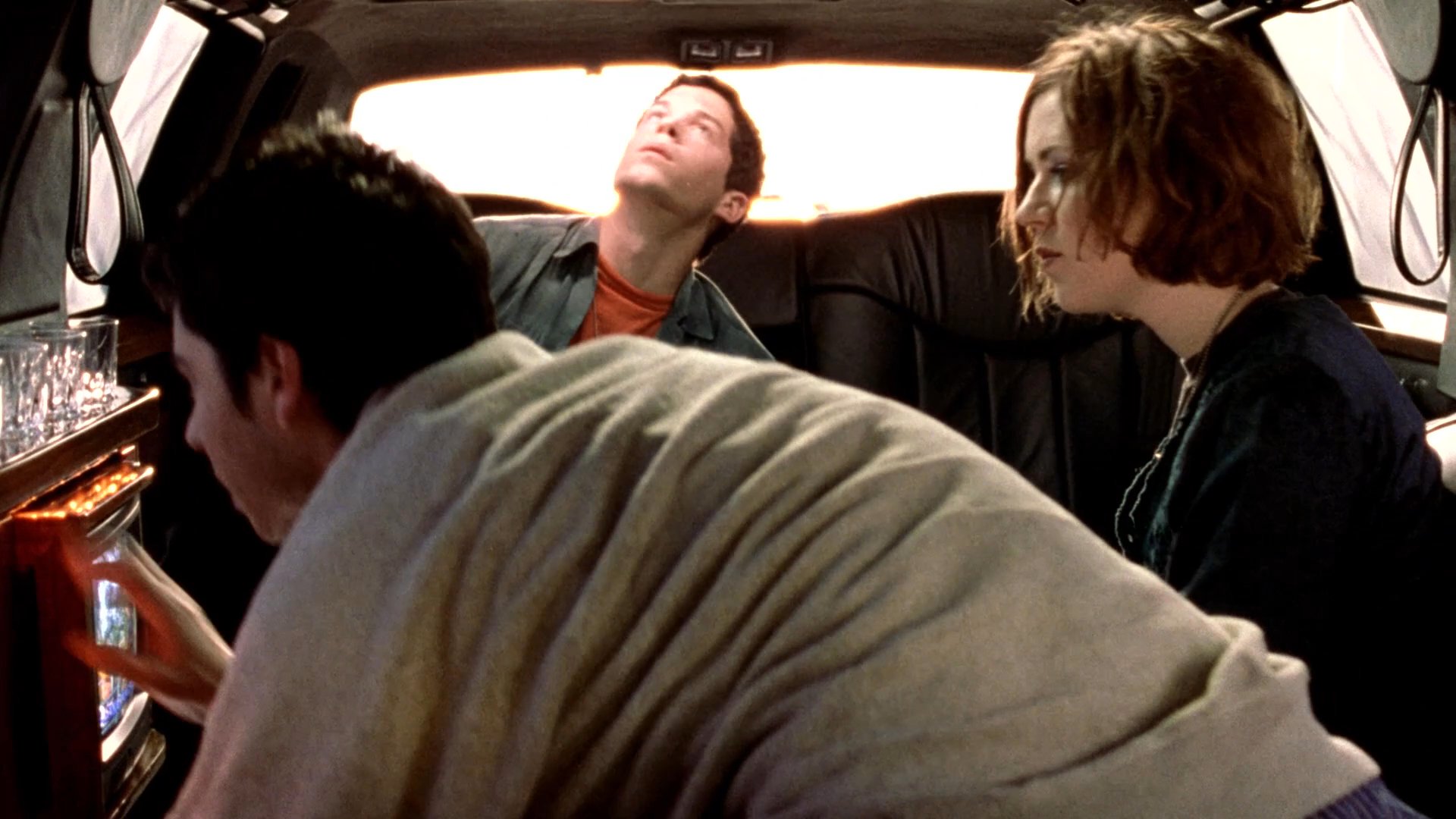 Two individuals conduct an interview inside a limousine while monitoring a live broadcast of a concert at Golden Gate Park on a small television.