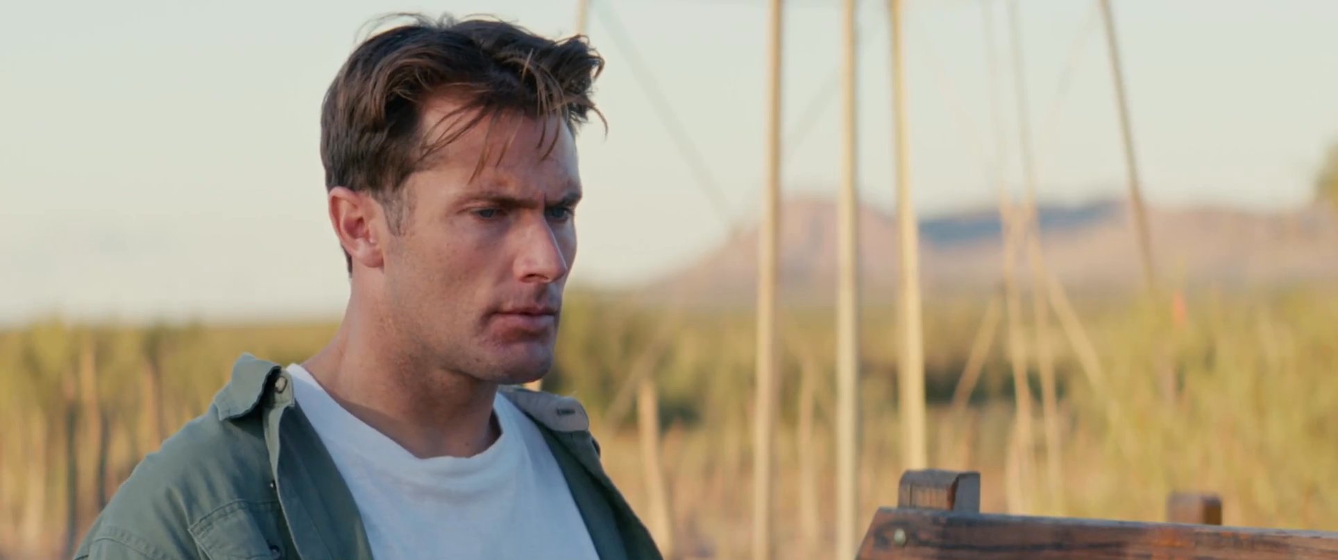 A man engages in a respectful conversation with a Native American elder beside an old pickup truck in a desert environment. The elder shares a feather as part of their interaction.