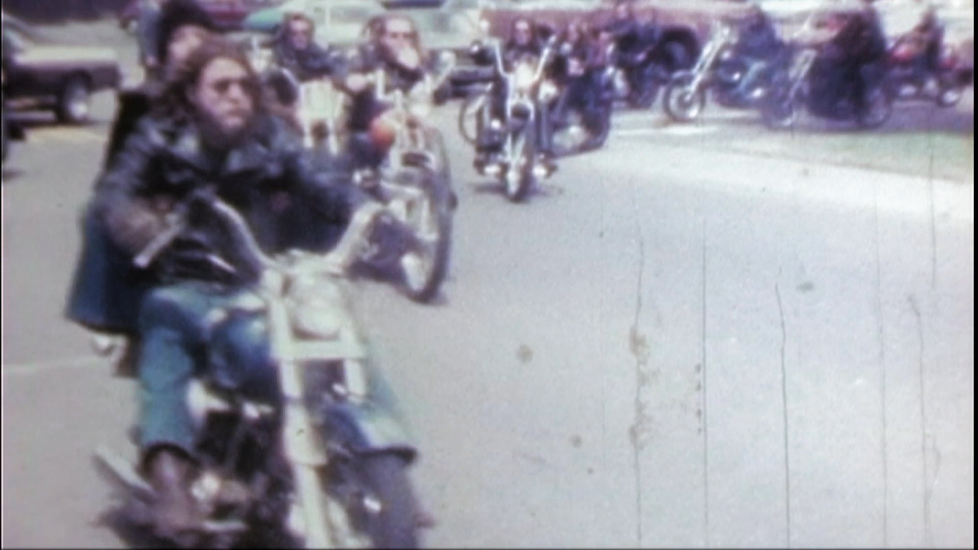 A large group of motorcyclists ride in a procession along a paved road. The riders wear leather gear and operate various styles of cruisers and motorcycles during a coordinated rally.