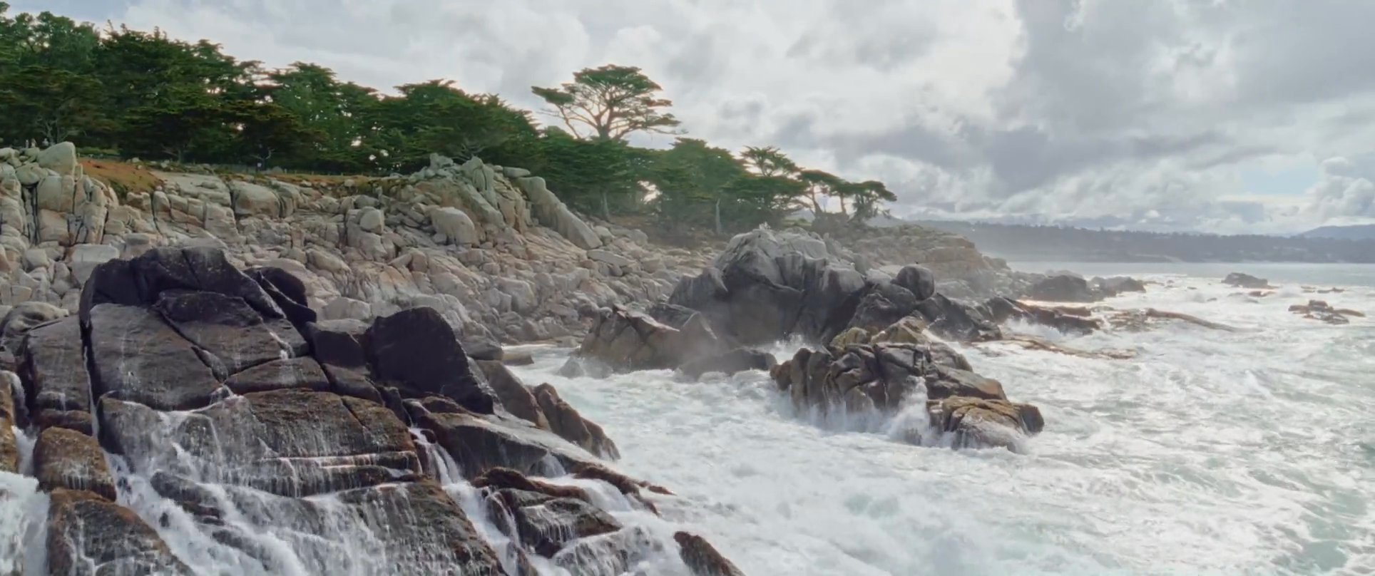 A surfer observes the powerful coastal surf at Ghost Trees before examining their own reflection in a calm tide pool. The scene captures the dramatic contrast between the turbulent Pacific waves and the tranquil shoreline.