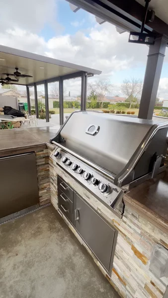 Outdoor kitchen with stone veneer base and built-in grill, sink, storage, and smoker