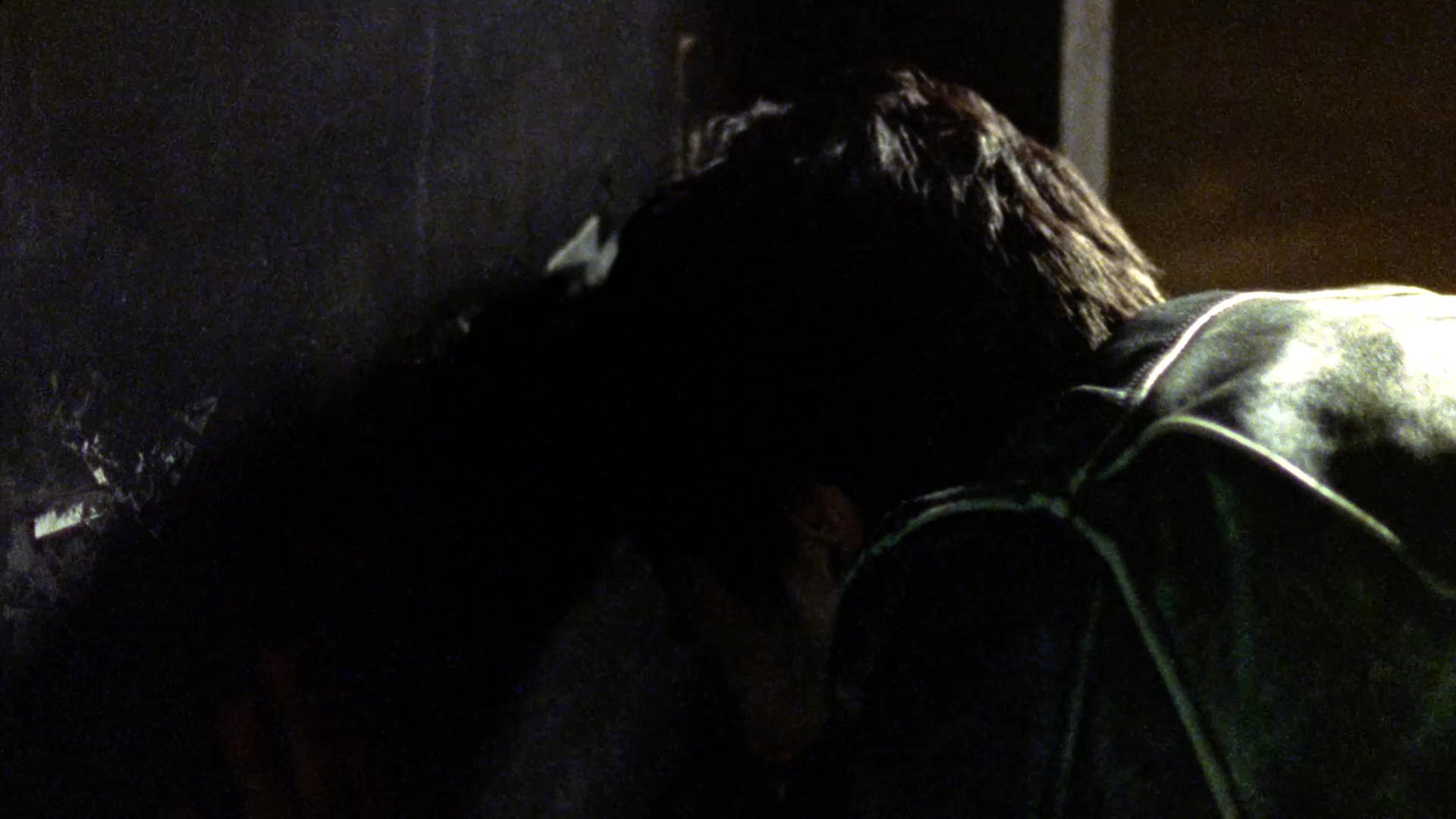 A man in a leather jacket appears distressed and presses his head against a wall in an outdoor night setting. He subsequently has a brief, tense interaction with another individual on the street.