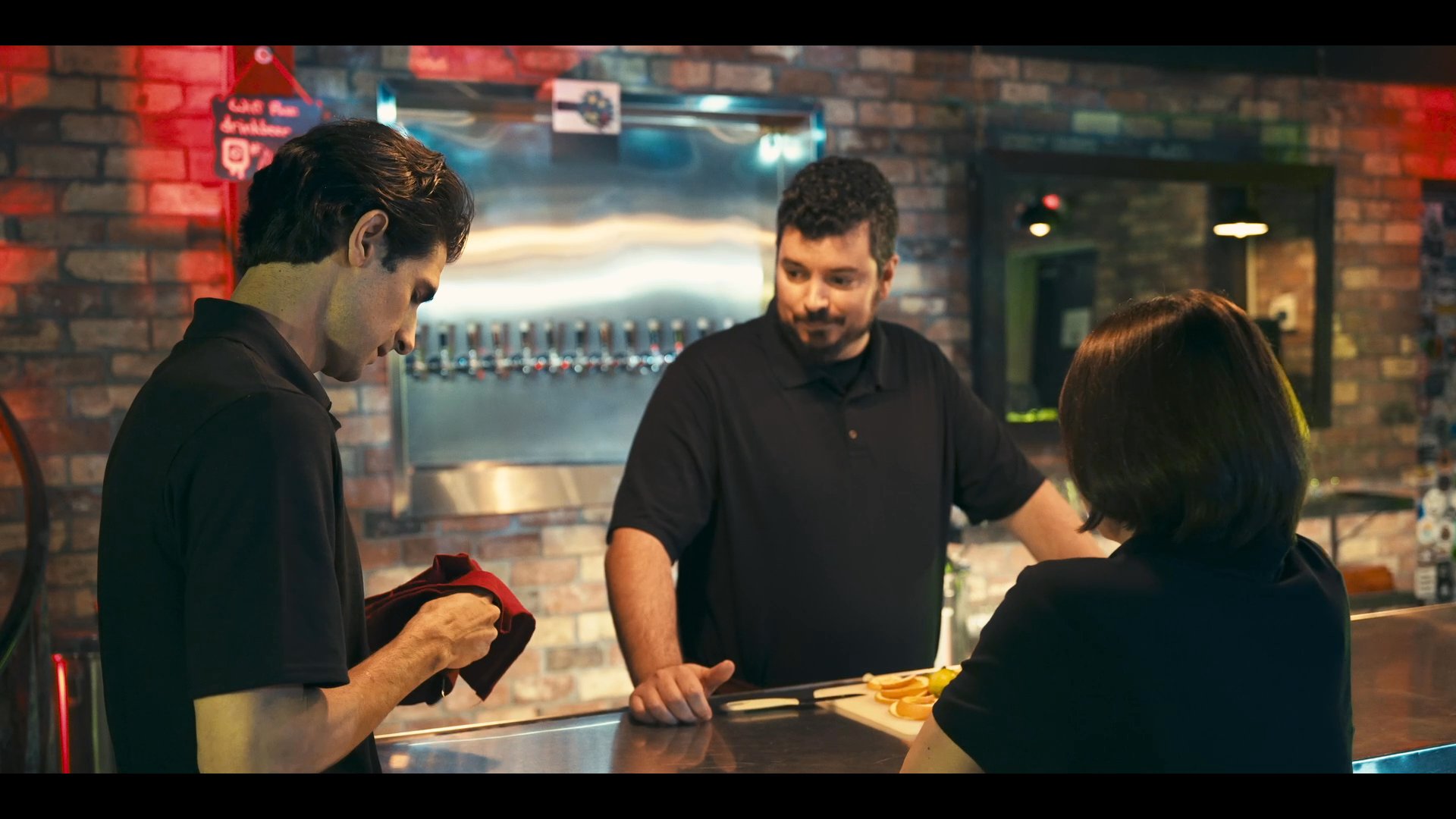 Brewery staff members discuss operations and food service preparations within an industrial brewing environment. The team coordinates tasks behind the bar and kitchen area to ensure professional service.