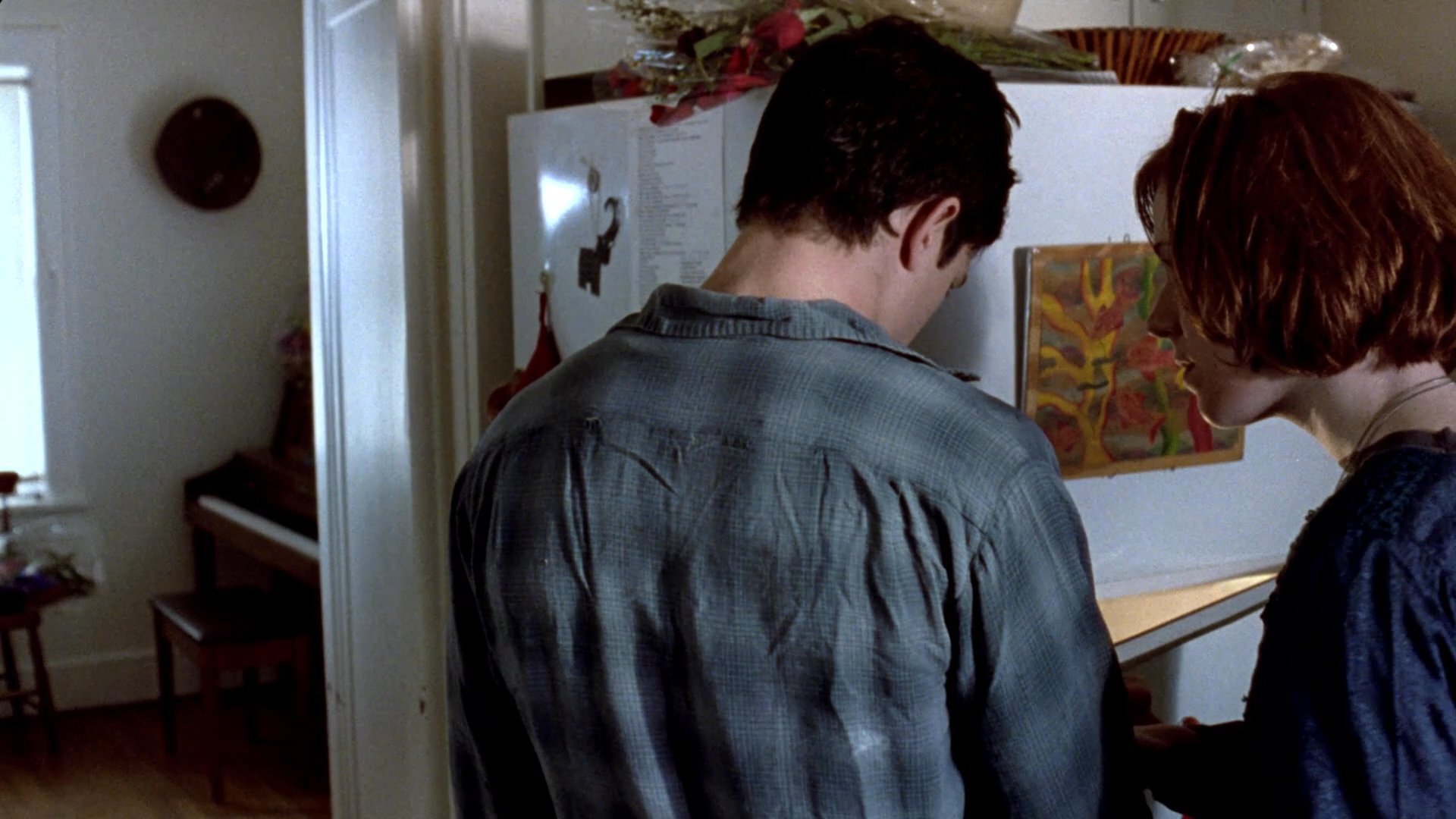 Two individuals console a man in his home following a loss, evidenced by a bouquet of flowers and supportive conversation. The atmosphere is quiet and somber as they navigate the difficult shared moment.