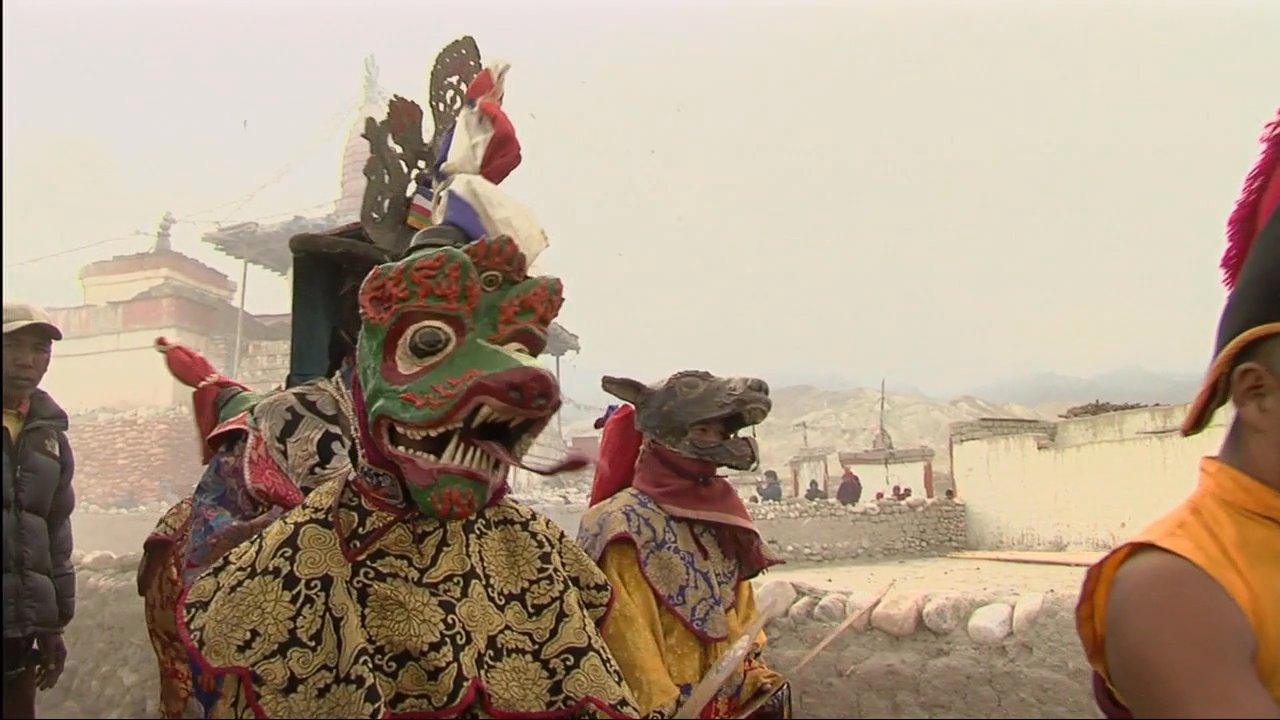 Tibetan monks perform a traditional cham dance in a monastery courtyard while musicians play cymbals and other ceremonial instruments.