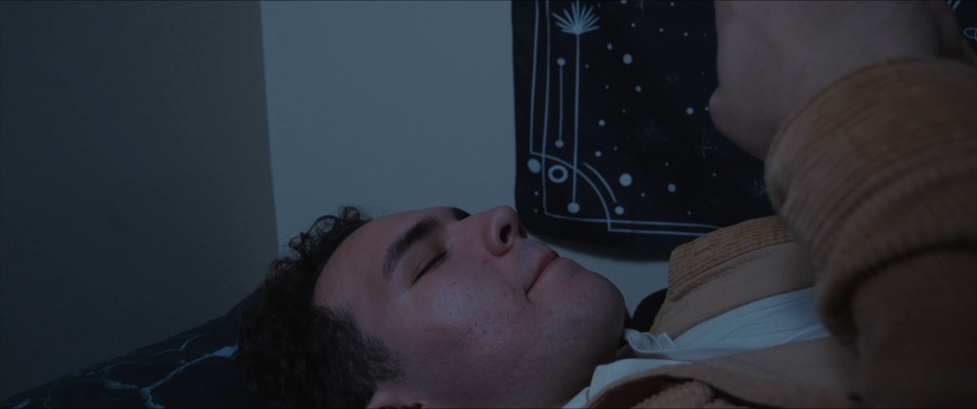 A person lies in bed and interacts with a messaging application on their smartphone while social media content plays in the background.