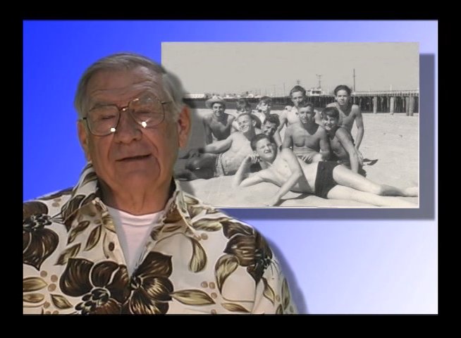 An older man shares personal reflections while a vintage black-and-white photograph of a family beach day is displayed beside him. The visual juxtaposition highlights the intersection of personal narrative and historical documentation.