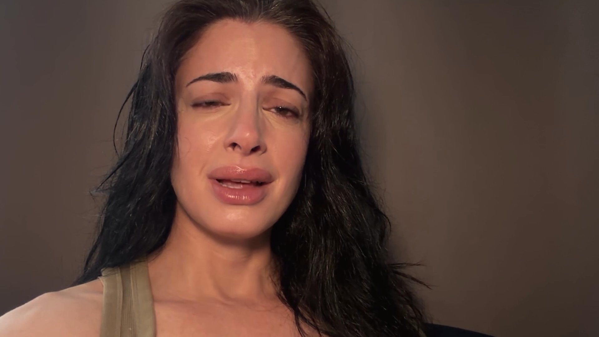 A woman exhibits visible signs of deep distress and sorrow, demonstrating a range of intense, mournful facial expressions in a minimalist setting.