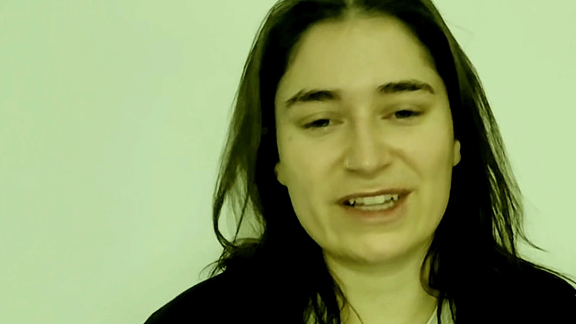 A woman delivers a monologue while speaking directly to the camera against a plain background. Her facial expressions and mouth movements indicate active engagement in conversation.