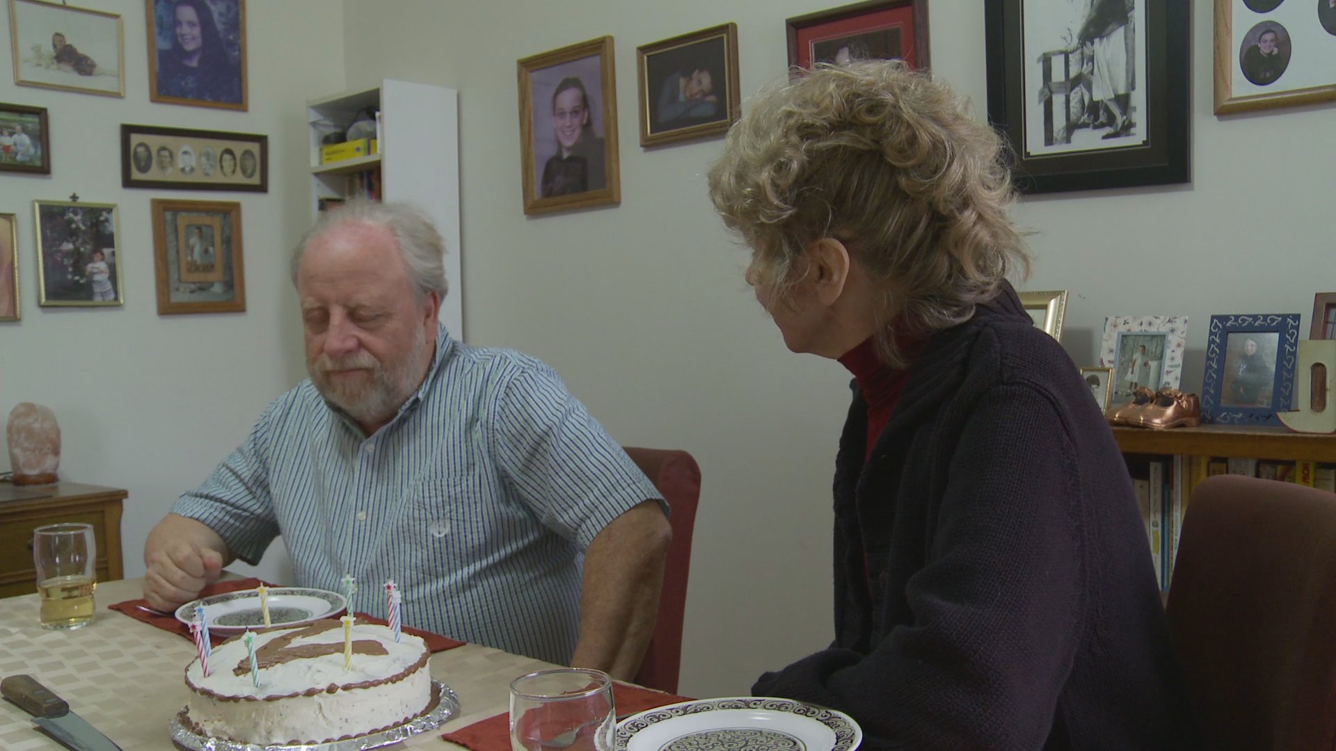 A man and woman share an intimate birthday celebration at a dining table, featuring a cake with lit candles and a final celebratory toast with glasses.