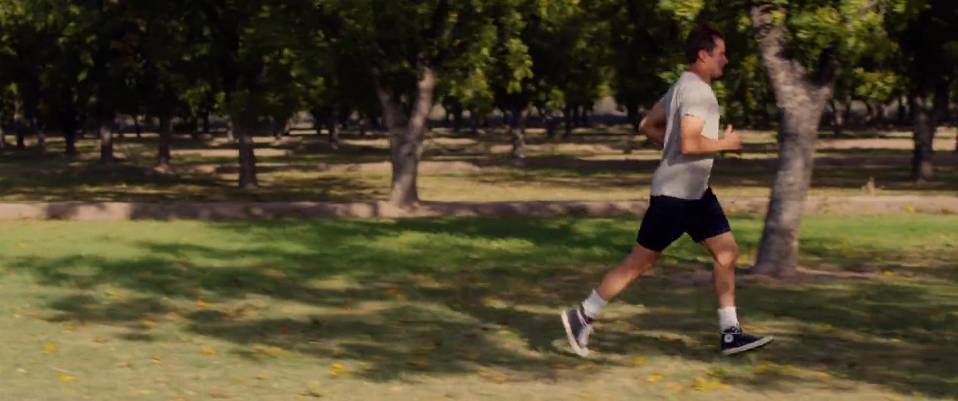 A man engages in a steady jog through a tree-lined park while interspersed shots of rushing water emphasize a sense of fluid motion. The scene captures an active lifestyle amidst a calm, natural environment.